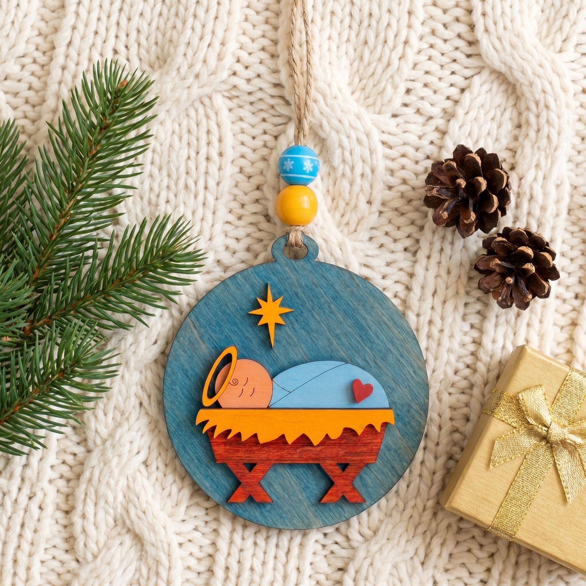 Baby Jesus wooden Christmas ornament flat-lay on cream knit blanket with pine and pinecones
