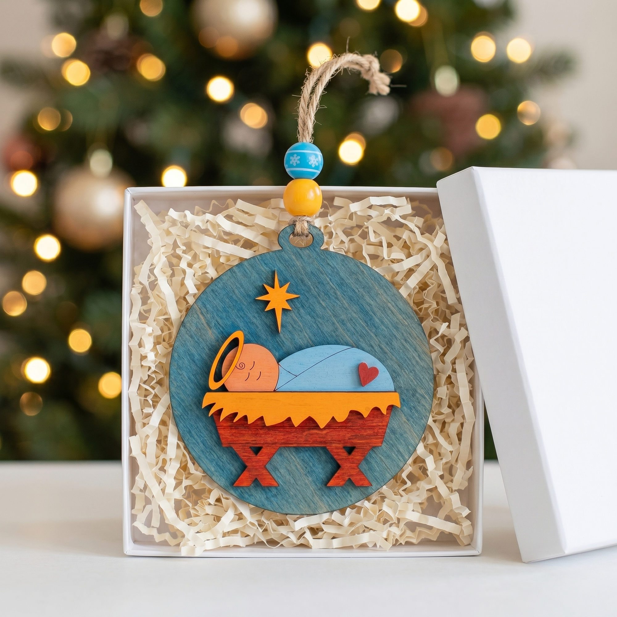 Baby Jesus wooden Christmas ornament standing in an open white gift box with shredded paper