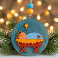 Baby Jesus nativity wooden Christmas ornament resting on a green pine branch with warm bokeh