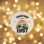 Personalized couples ceramic Christmas ornament hanging against warm golden holiday bokeh