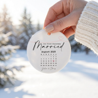 Hand holding a personalized First Christmas Married calendar ceramic ornament with a snowy background