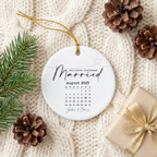 First Christmas Married calendar ceramic ornament flat-lay on a cream knit blanket with pinecones