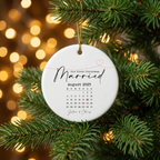 First Christmas Married August 2025 calendar ceramic ornament nestled in pine branches with golden Christmas lights