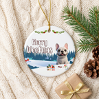 Merry Woofmas frenchie ceramic ornament for Mojo, flat-lay on a cream knit blanket with pinecones