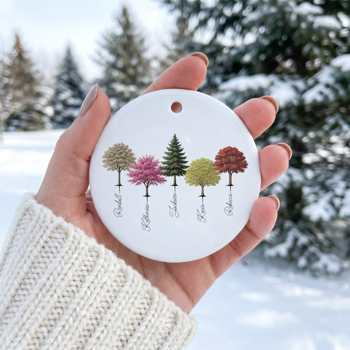 Hand holding a personalized My Forest family tree ceramic ornament with a snowy background