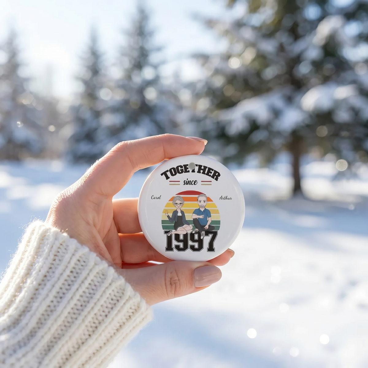 Hand holding a personalized Together Since 1997 ceramic ornament with a snowy background